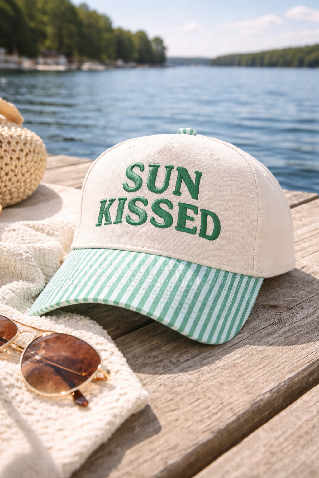 Cap with 'SUN KISSED' text on a wooden dock by a lake
